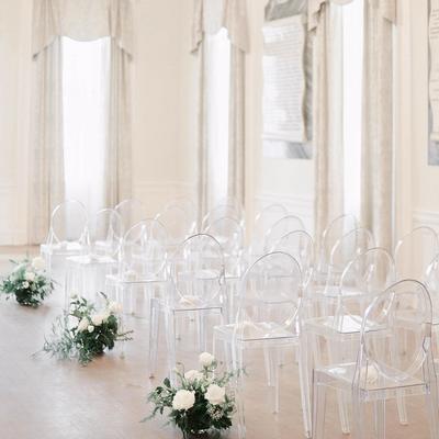Wedding ceremony area featuring clear ghost chairs and floral arrangements on the floor.