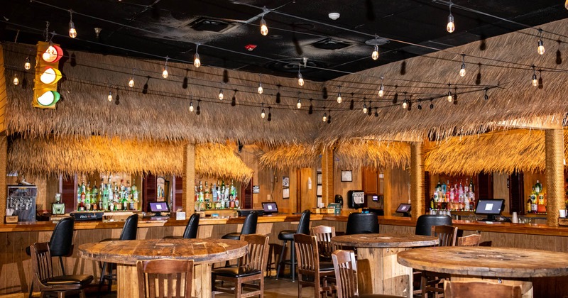 Interior, wooden tables, chairs, straw-covered counters, screens, bottles