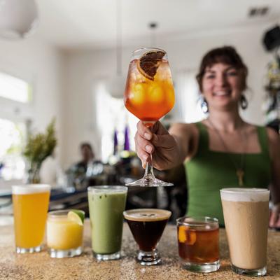 A smiling bartender holds Aperol Spritz over the counter with assorted cocktails.