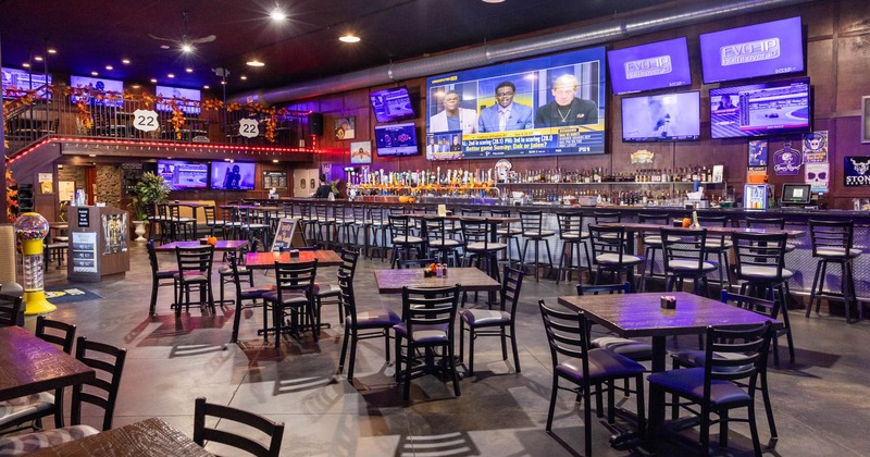 Interior, tables and chairs, long bar setup with drink shelves and TVs behind