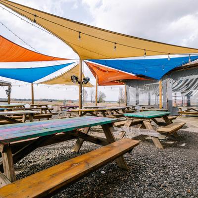 Outdoor seating area featuring picnic tables with benches, and sun shade sails.