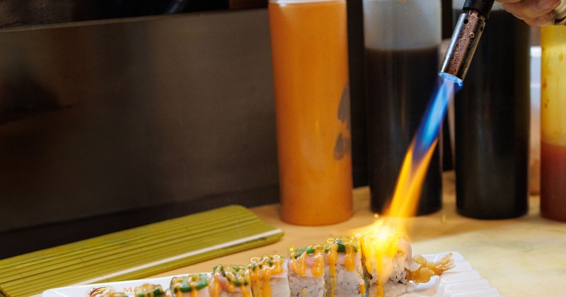 Sushi roll is being seared using a kitchen torch