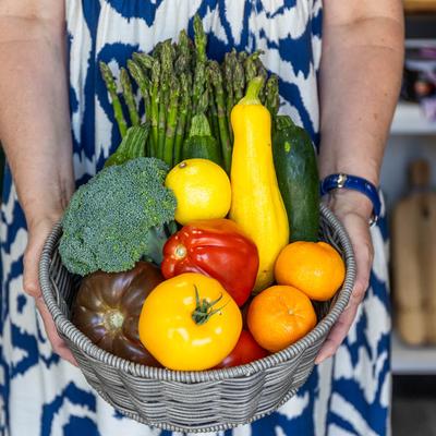 Hands holding a wicker basket with vegetables.