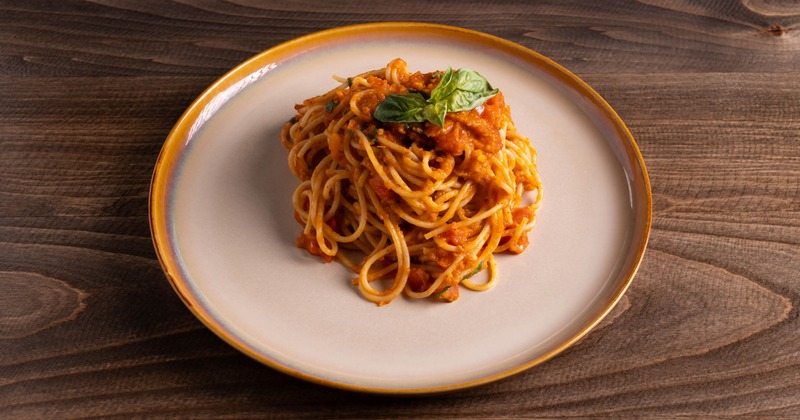 Spaghetti marinara on a white plate with basil garnish