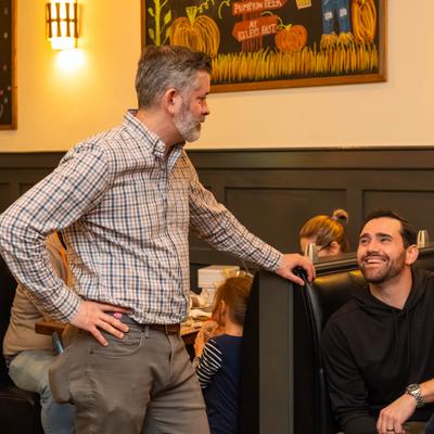 Restaurant staff member chatting with a smiling guest seated in a booth.
