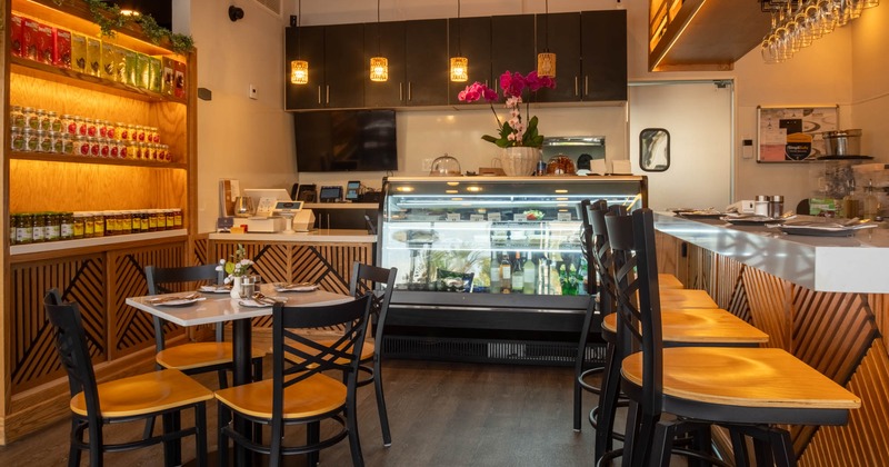 Cozy cafe interior with shelves, a display case, dining table, high counter, and pendant lights