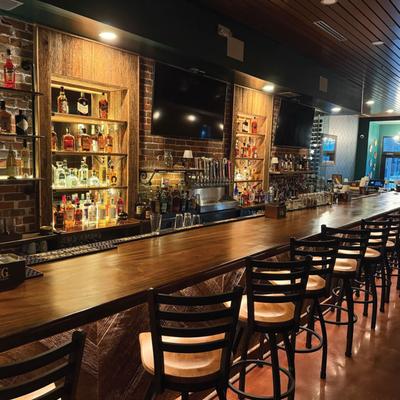 Inrterior of bar area with counter, bar stools, and shelves with various bottles.