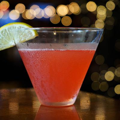 Red cocktail garnished with a lime wedge.