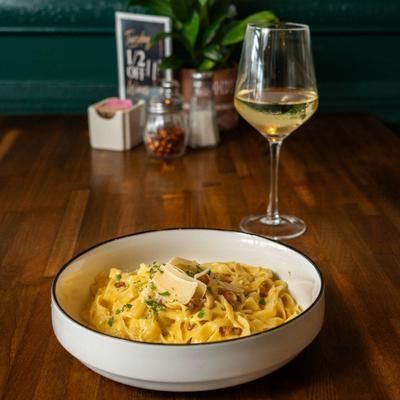 Fettuccine carbonara served with a glass of white wine on a restaurant table.