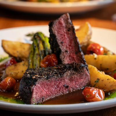 A hanger steak, served with roasted potatoes, asparagus, cherry tomatoes, and a sauce.