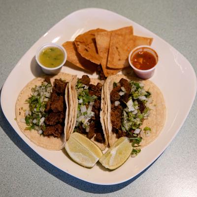 Tacos topped with cilantro, diced onion, and grilled meat, served with chips, salsa and lime.