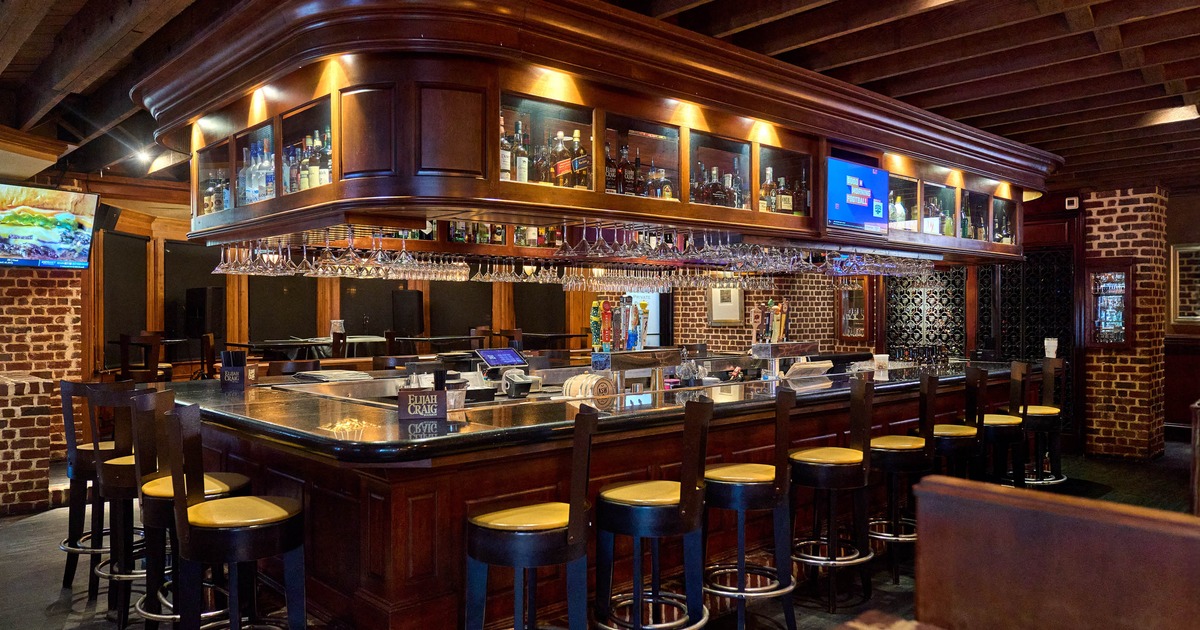 Bar interior - wooden counter, stools, overhead liquor display, hanging glasses and brick walls
