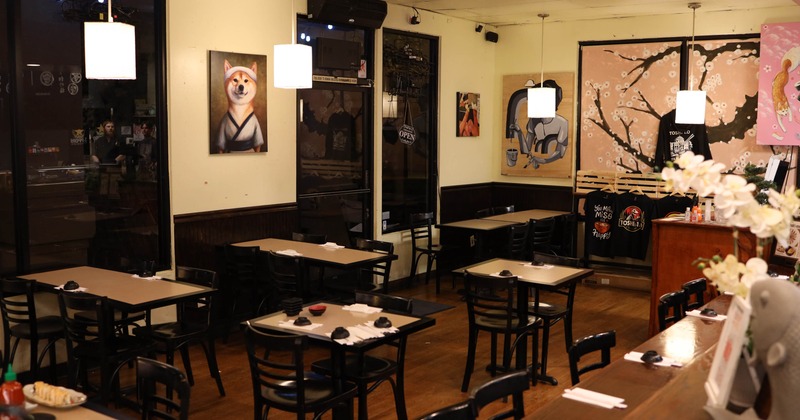 Interior of a restaurant with tables, chairs, paintings, and pendant lights