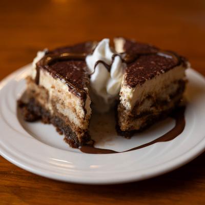 Two slices of tiramisu cake with whipped cream and chocolate drizzle.