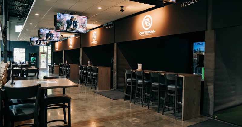 A room with golf simulator booths and seating