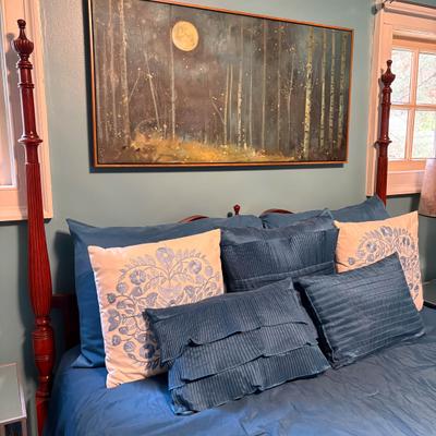 Bed with blue bedding, pillows, and moon forest wall art.