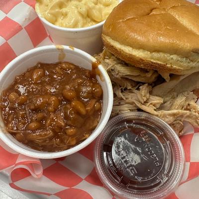 Pulled chicken sandwich on a bun, with mac and cheese, beans, and a sauce.