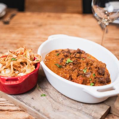 A bowl of beef stew served with mashed potatoes topped with fried onions.
