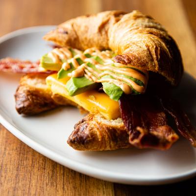 A croissant sandwich with bacon, egg, cheese, avocado and our house made sriracha aioli.