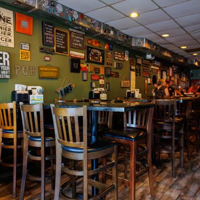 Interior with high-top tables and a green wall decorated with numerous signs and stickers.
