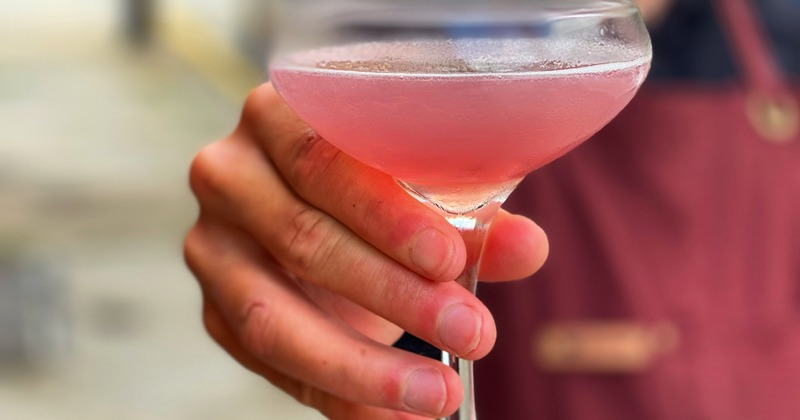This is a close up of a cocktail. Someone is holding the drink out in front of them.