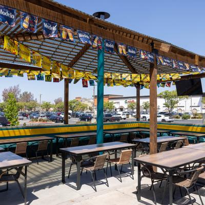 Outdoor patio with wood-framed pergola overhead, adorned with various beer brand flags.