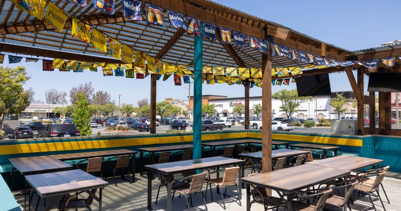 Outdoor patio with tables, chairs, and beer banners under a wooden pergola.