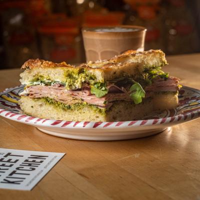 A focaccia mortadella sandwich with pesto and arugula.