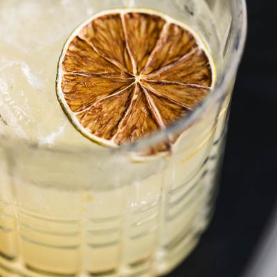 Yuzu Whisky Sour cocktail garnished with dried lime wheel, close-up.