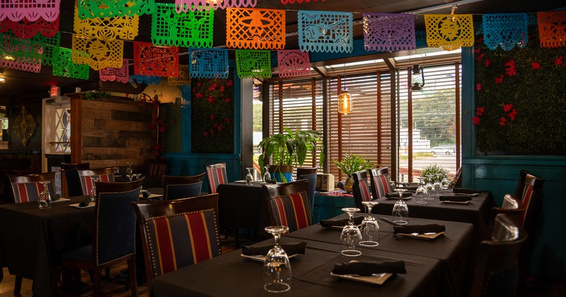 Interior of cozy Mexican-style restaurant, dining area decorated with hanging paper ornaments