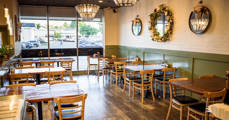Interior with wooden tables and chairs, floral wall decorations, and large windows allowing natural light