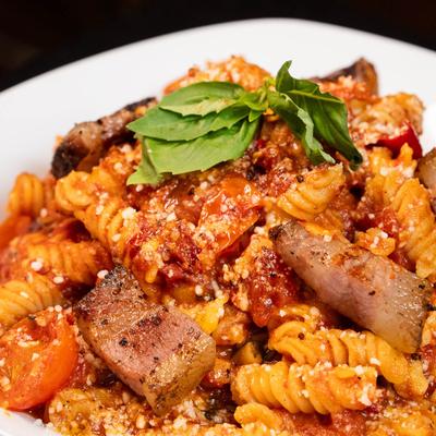 Pasta with spicy tomato sauce, peppers, basil, and cured meat.