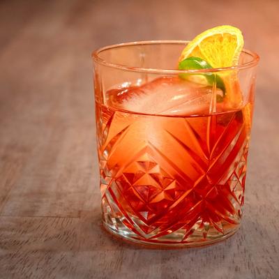 Vibrant red cocktail in a low, cut-glass tumbler with a large ice cube.