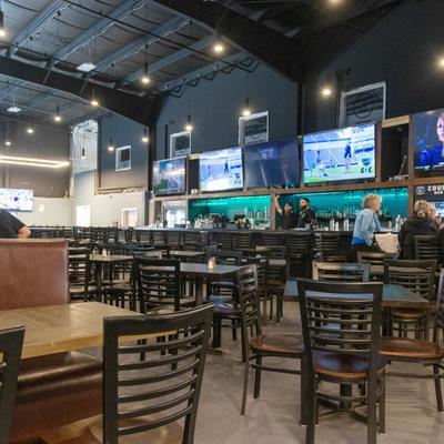 Spacious interior, seating area with booths, tables and chairs, a bar with screens.