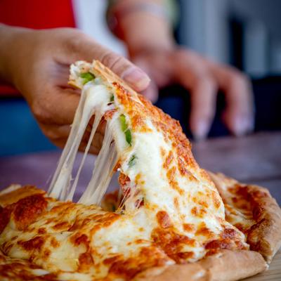 A person pulling a slice of calzone, which has a melted cheese topping.
