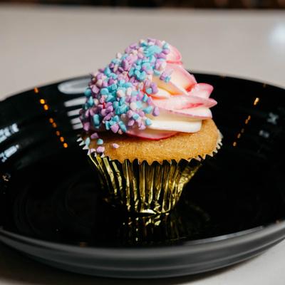 A cupcake with pink and white frosting and colorful sprinkles on a black plate.