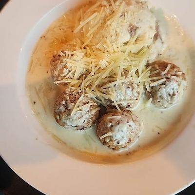 Meatballs in creamy sauce topped with shredded cheese.