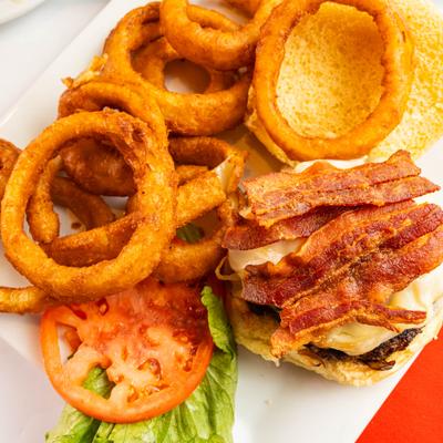 Bacon cheeseburger served alongside a side of onion rings, lettuce, and a tomato slice