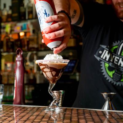 Bartender topping a cocktail in martini glass with whipped cream.