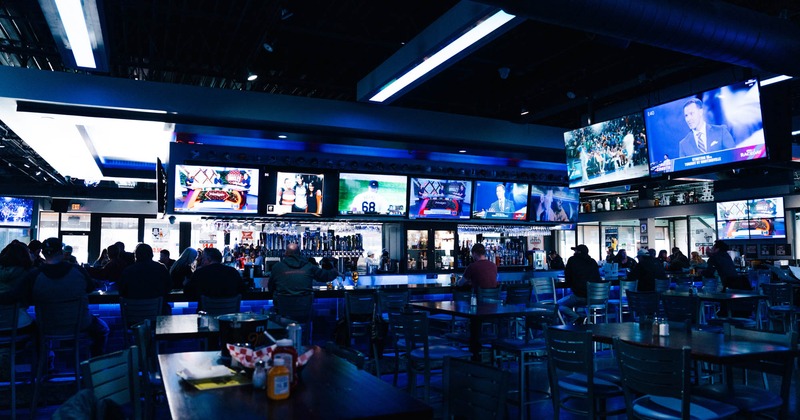 A lively sports bar scene featuring guests seated at bar counter, watching sports on screens