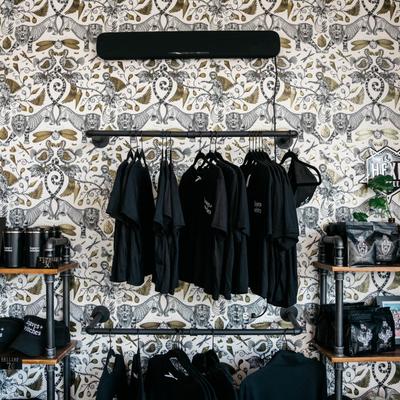Merchandise display with T-shirts and tumblers against a patterned wallpaper backdrop.