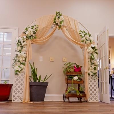 Decorated wedding arch flanked by two white lattice stands and two potted plants.