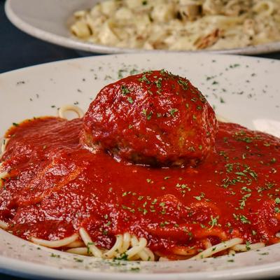 Spaghetti topped with marinara sauce and a large meatball.