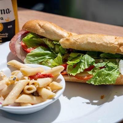 Italian sub served with pasta salad and a bottle of beer.
