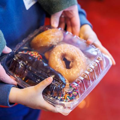A child holding a clear plastic container filled with assorted donuts.