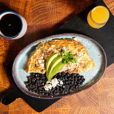 Omelet topped with sliced avocado, served with black beans, coffee, and orange juice.