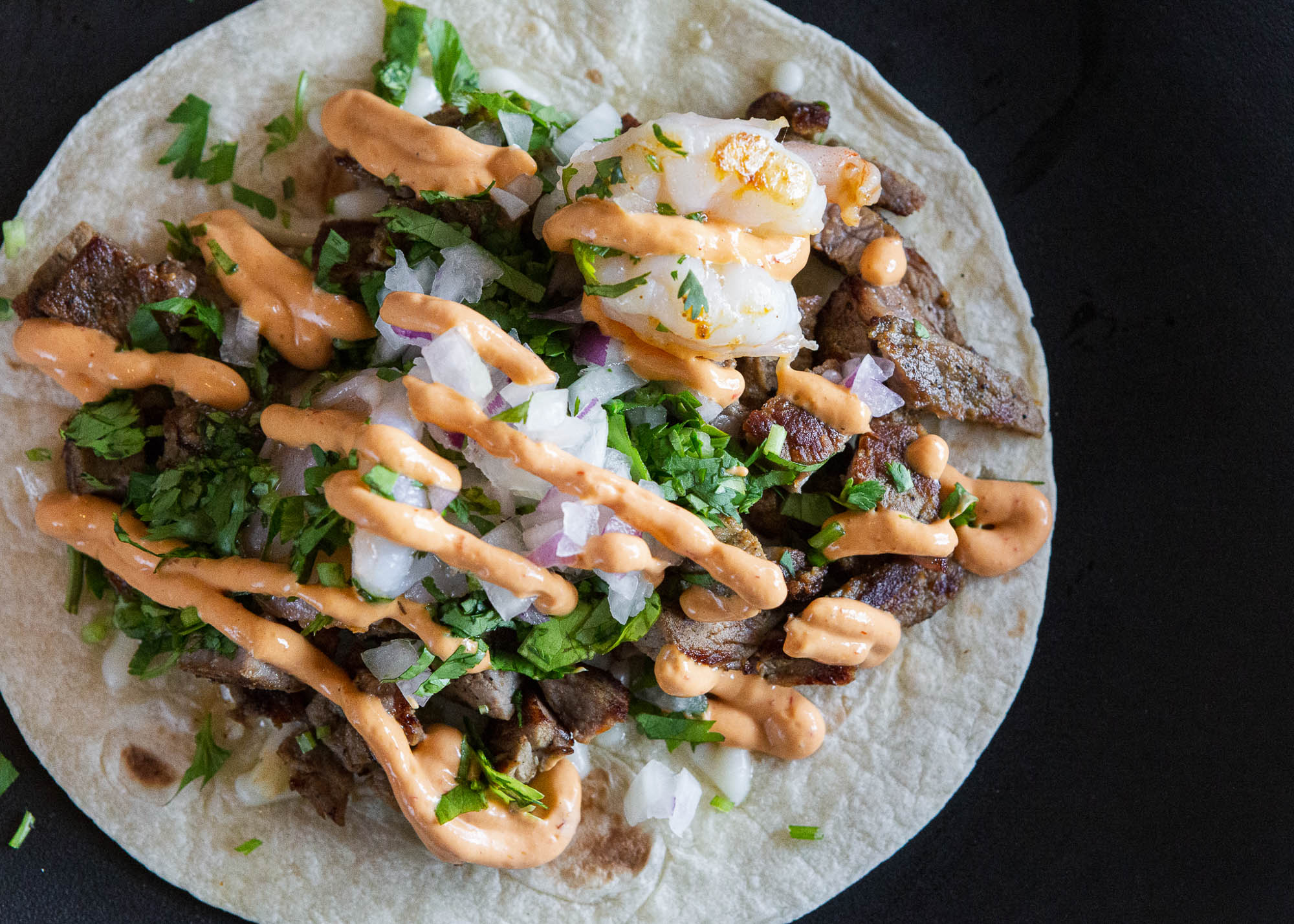 Surf & Turf taco, topped with cheese, onion, cilantro and chipotle crema