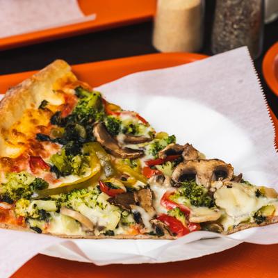 A slice of broccoli pizza with mushrooms.