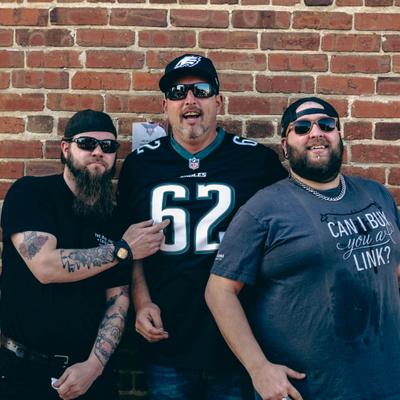 Three persons posing in front of the brick wall.