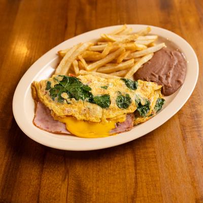 Folded cheese, ham, and spinach omelet served alongside fries and refried beans.